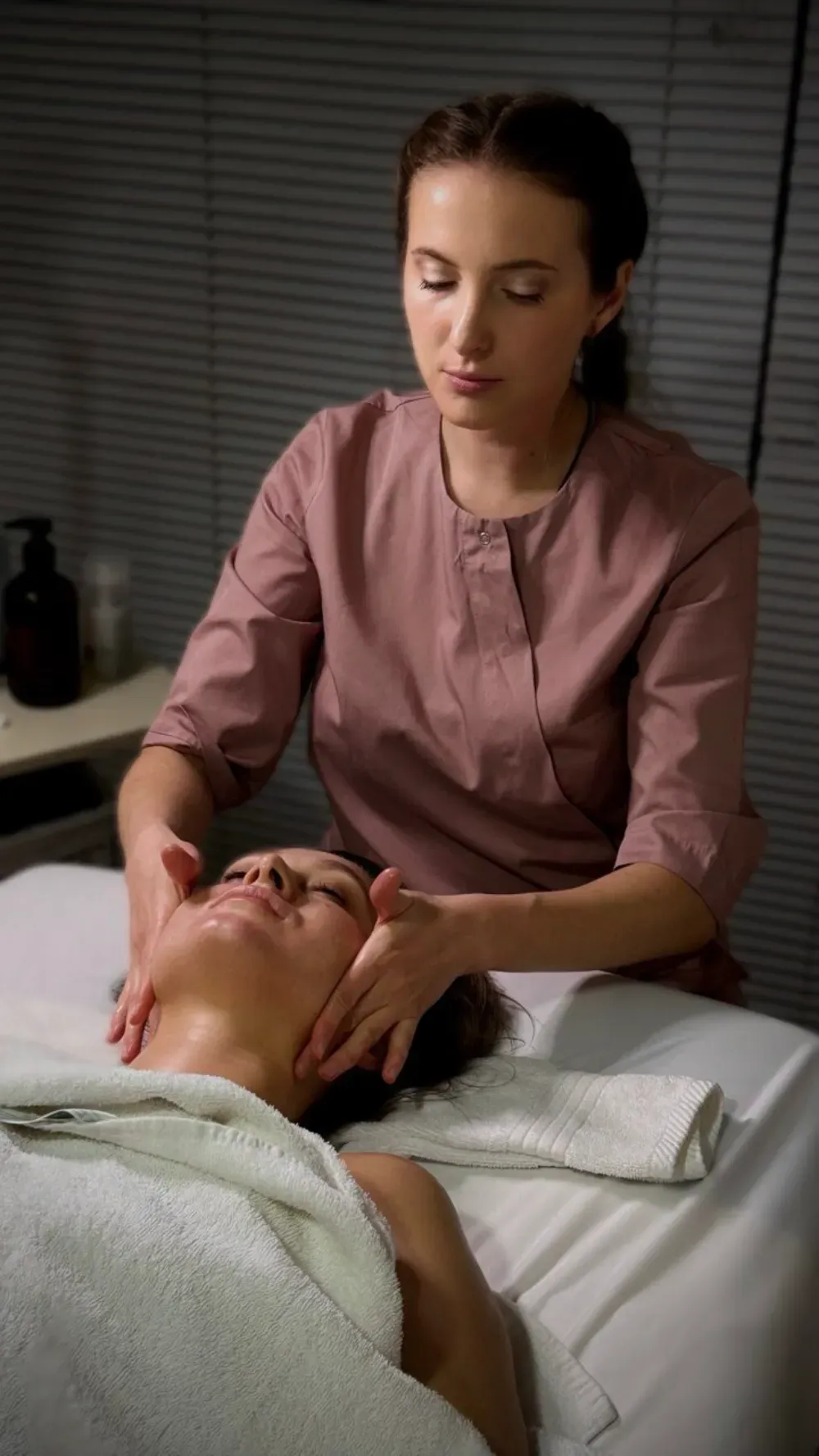 Una profesional le da un masaje facial a una clienta que yace en una camilla de masaje en un ambiente de spa