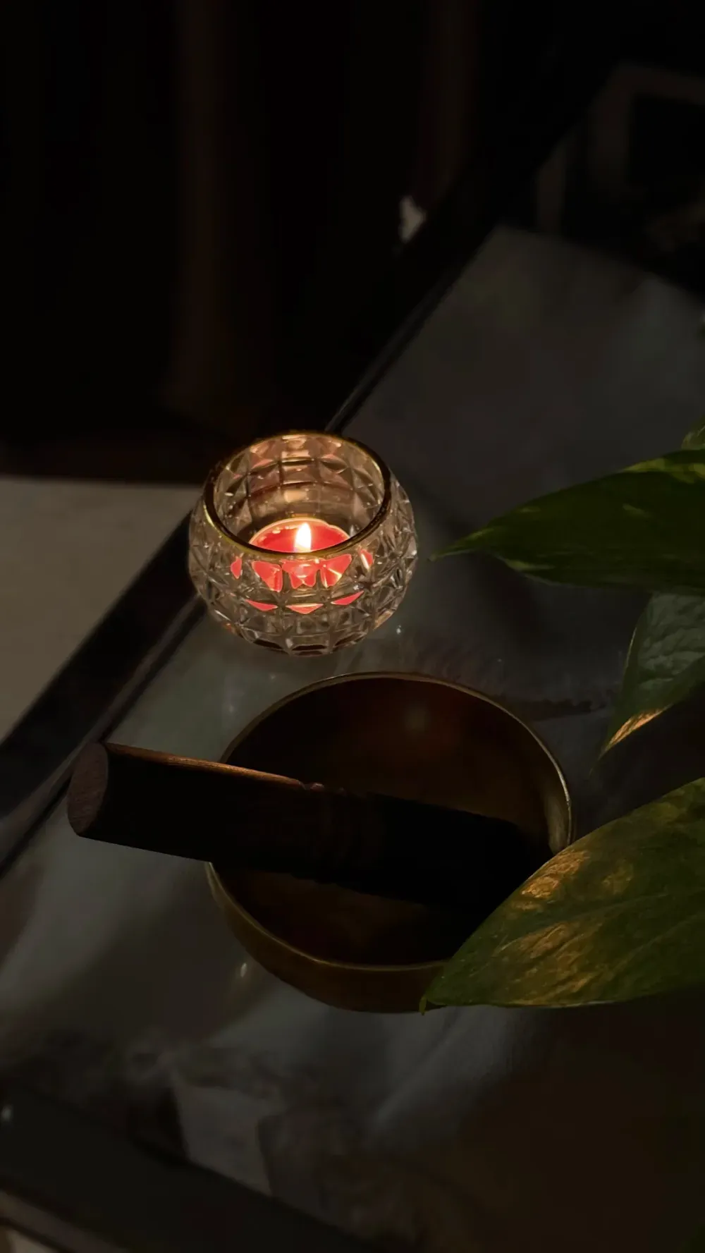 Una vela encendida en un portavelas de cristal decorado, junto a un cuenco tibetano con un mazo