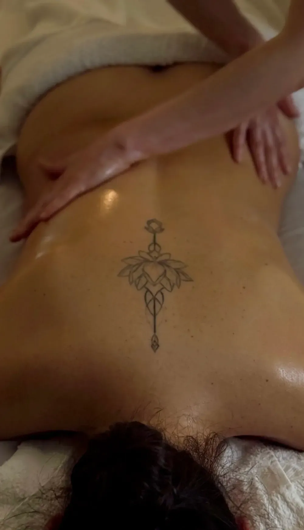 Una persona recibe un masaje de espalda, que incluye un tatuaje detallado de una flor de loto de líneas finas