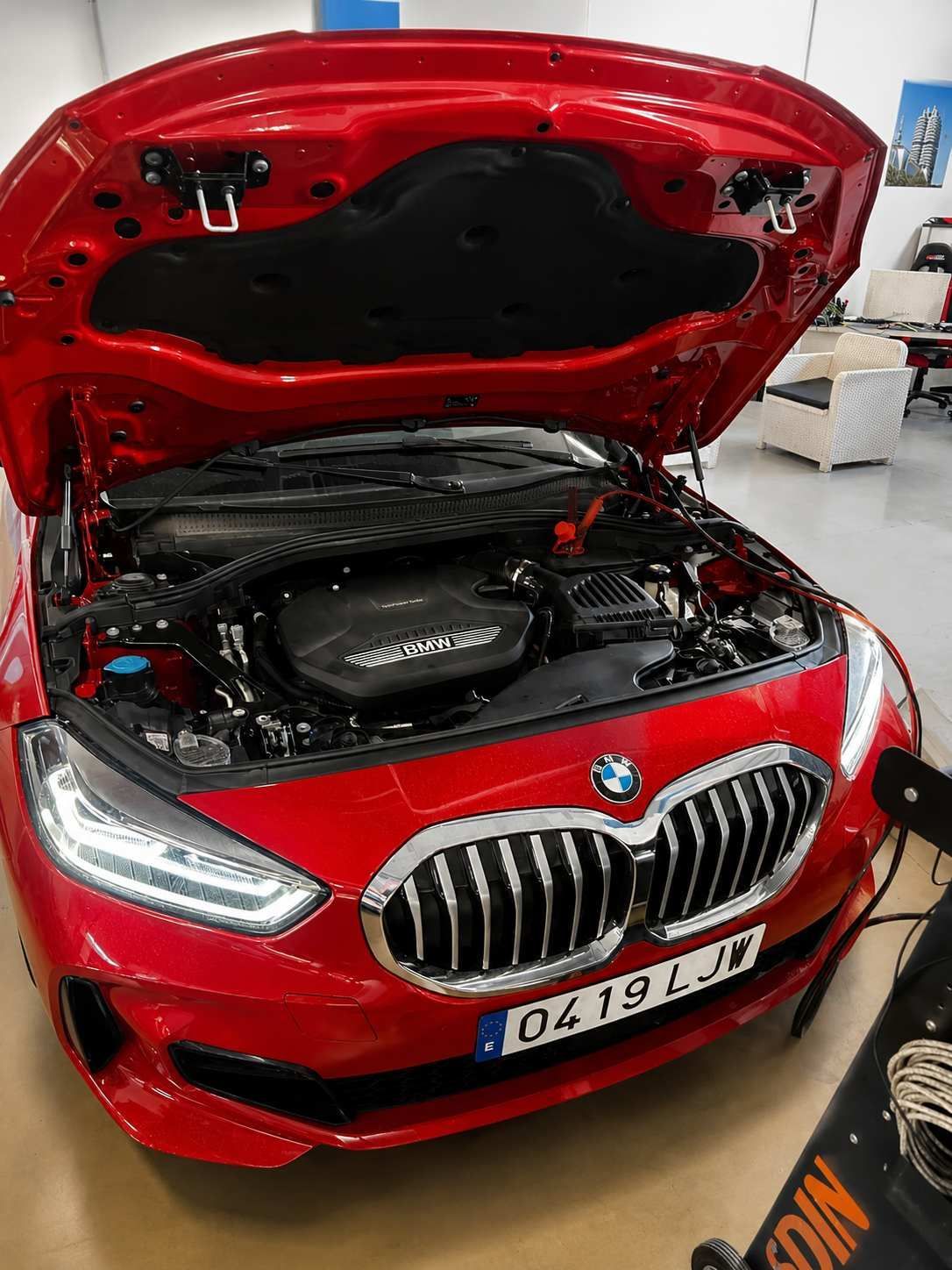 BMW rojo con el capó abierto, mostrando el motor en un garaje.