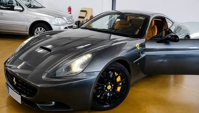 Coche deportivo gris con llantas negras expuesto en el interior, puerta del conductor abierta.