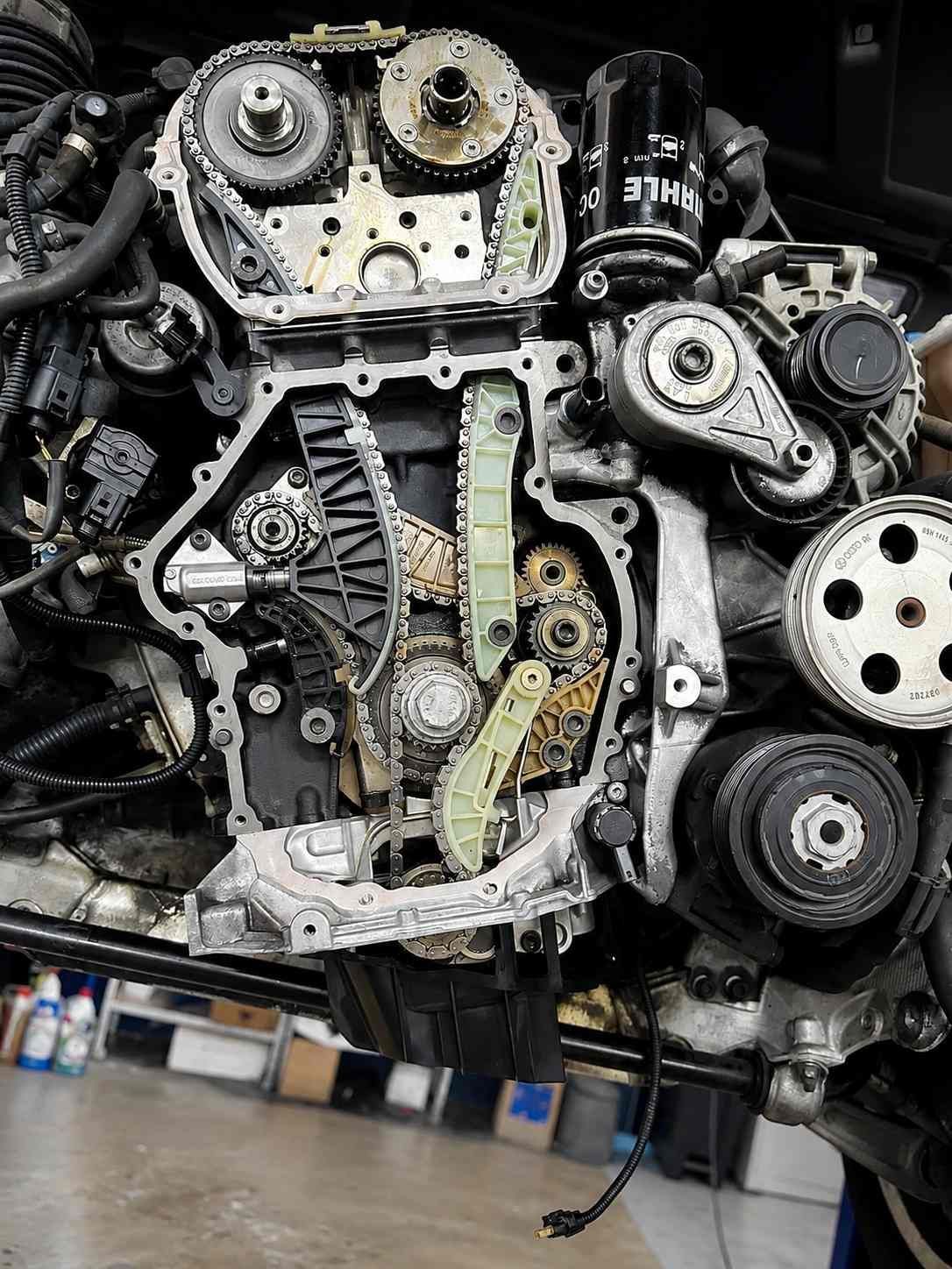 Primer plano de un motor expuesto con correas, engranajes y componentes metálicos en un taller.