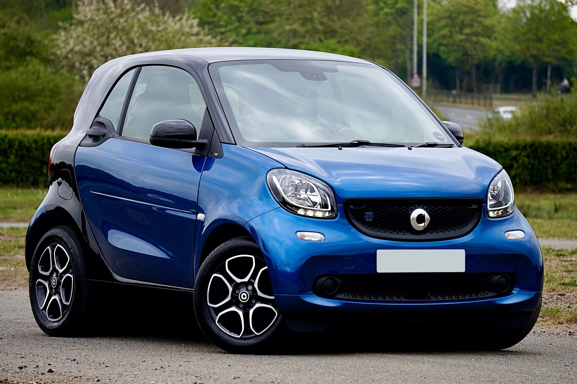 Coche Smart azul aparcado en una carretera con árboles al fondo.