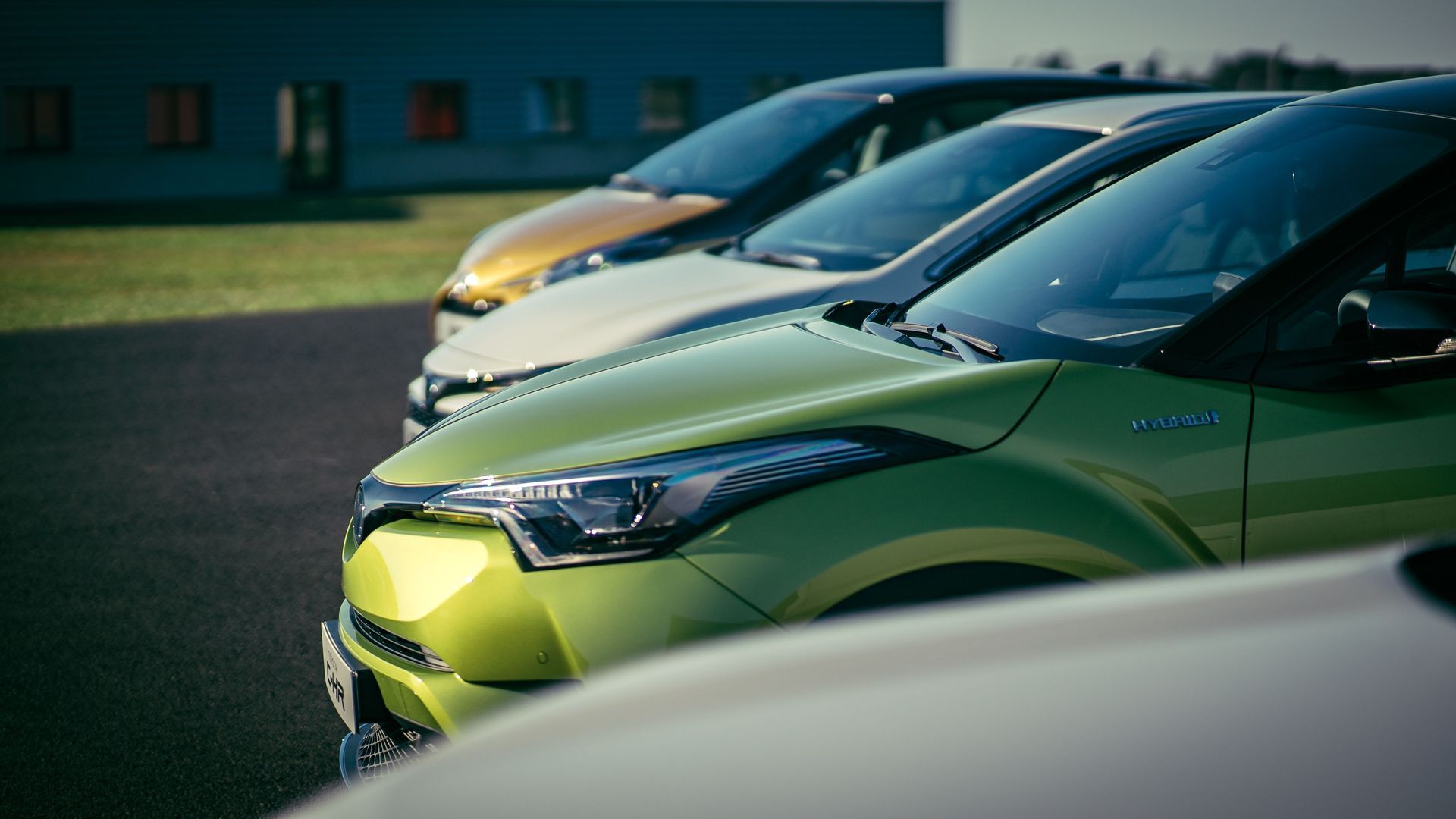 Fila de coches aparcados, incluyendo un coche de color verde brillante delante, vistos de lado en un aparcamiento.
