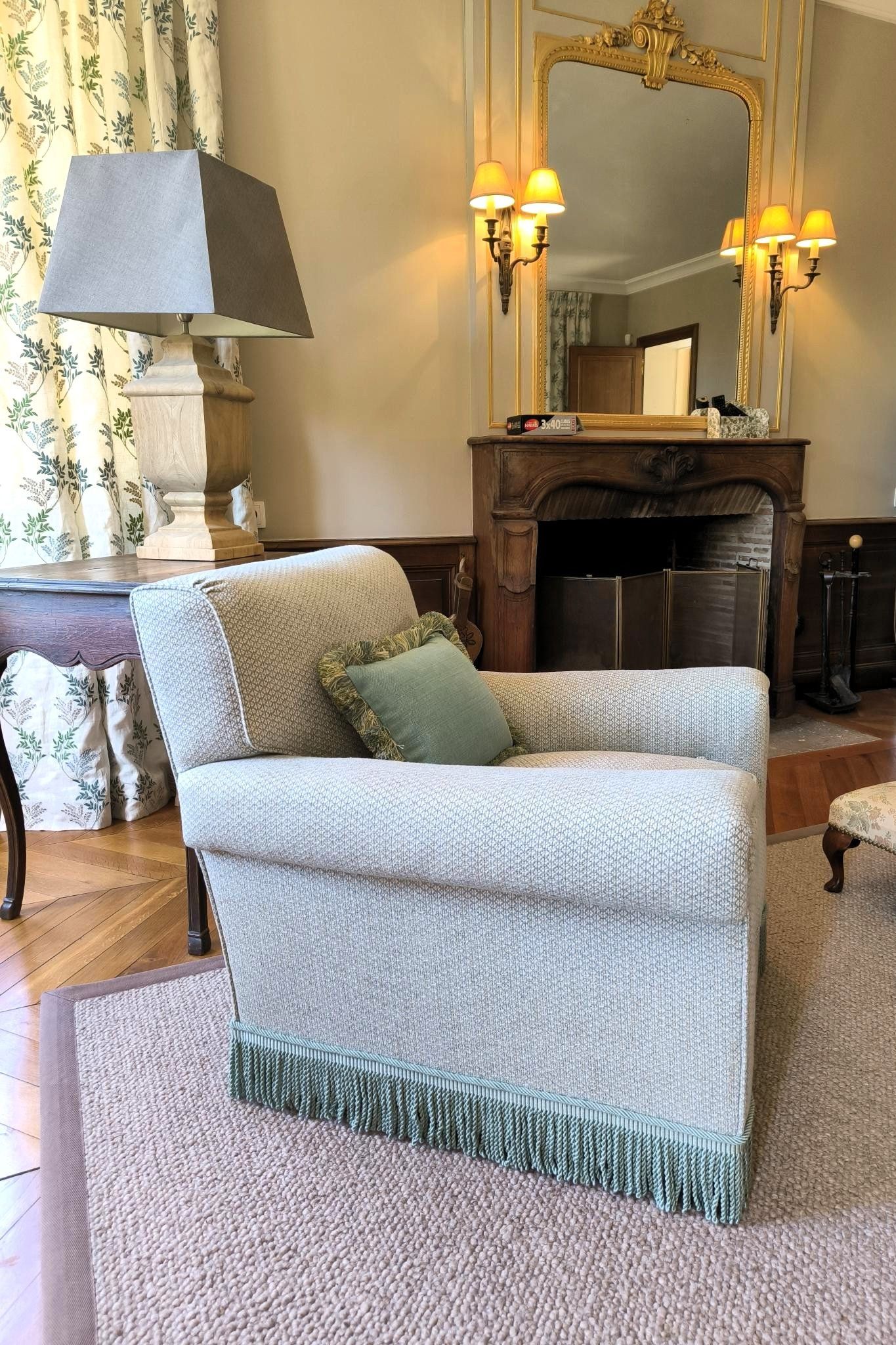 Salon cosy avec fauteuils couleur crème, cheminée en marbre, miroir orné et moquette rose pâle.