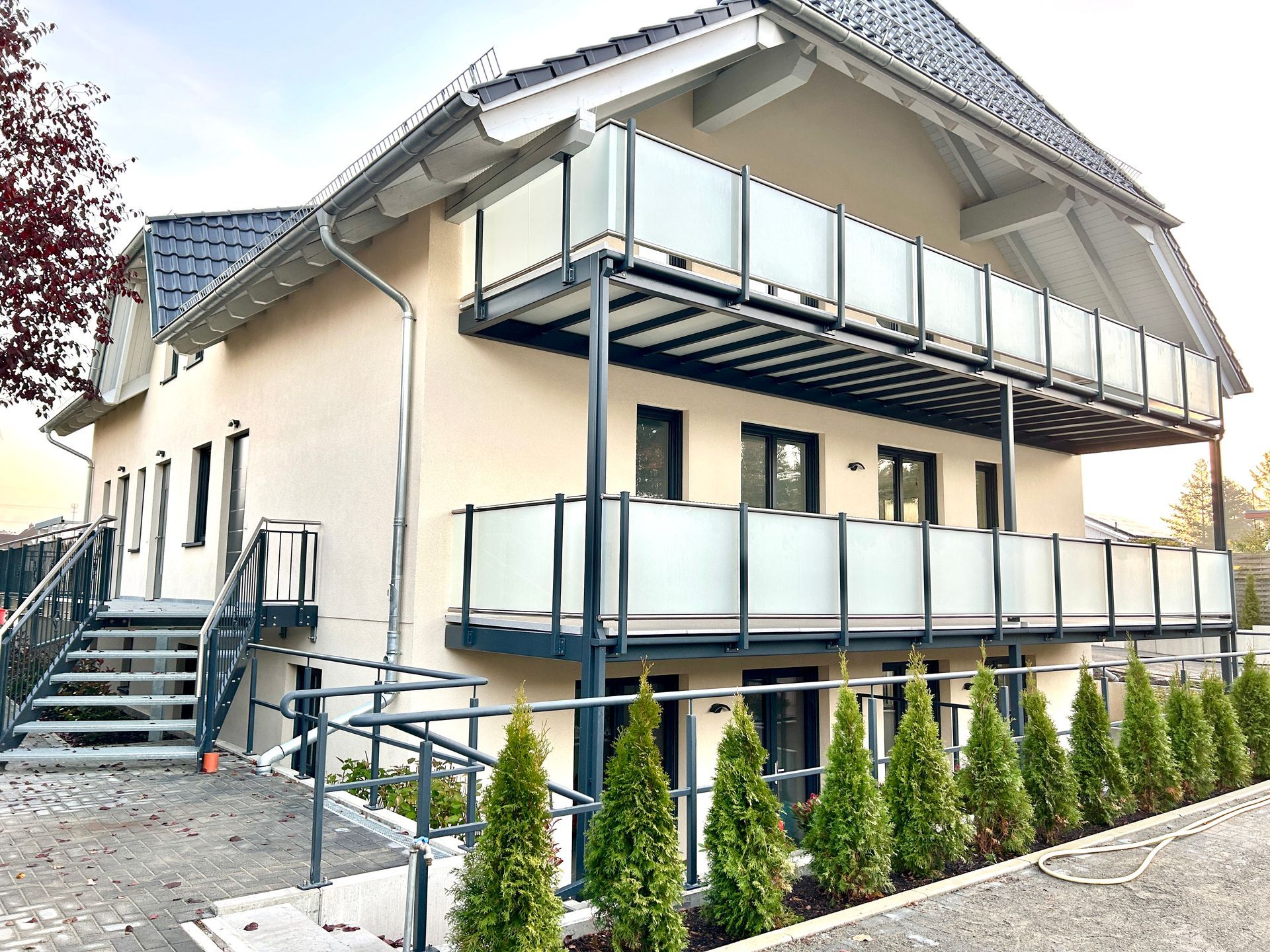 Zweistöckiges Gebäude mit Balkonen, dunklem Dach, hellen Wänden und einer Rampe für barrierefreien Zugang.