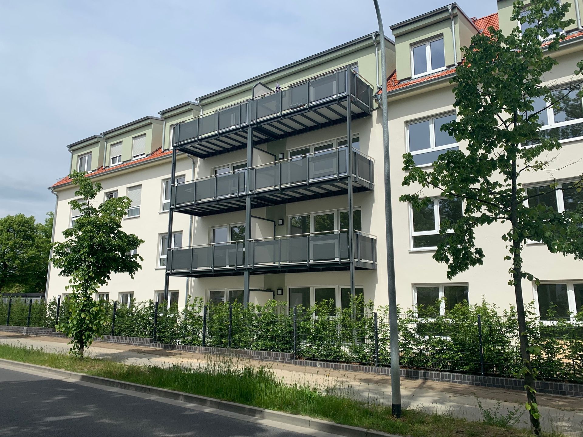 Mehrstöckiges Wohnhaus mit Balkonen, grünem Laub und blauem Himmel.