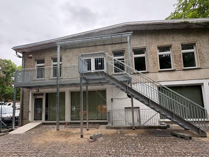 Außenansicht eines Gebäudes mit Metalltreppe und Balkon als Zugang. Graues Gebäude mit Fenstern.