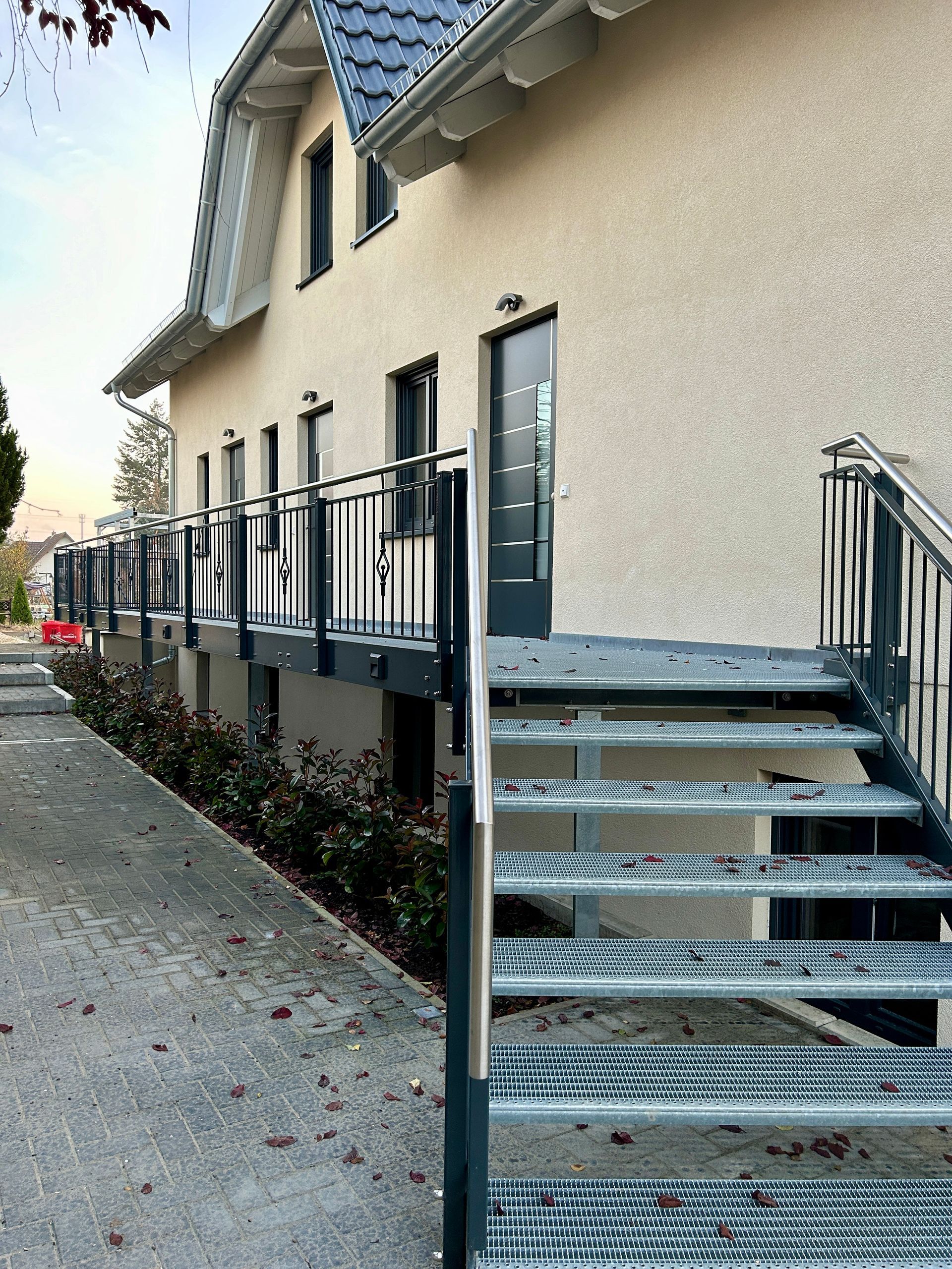 Außenansicht eines Gebäudes mit einer Metalltreppe, die zu einer erhöhten Plattform und Eingangstüren führt