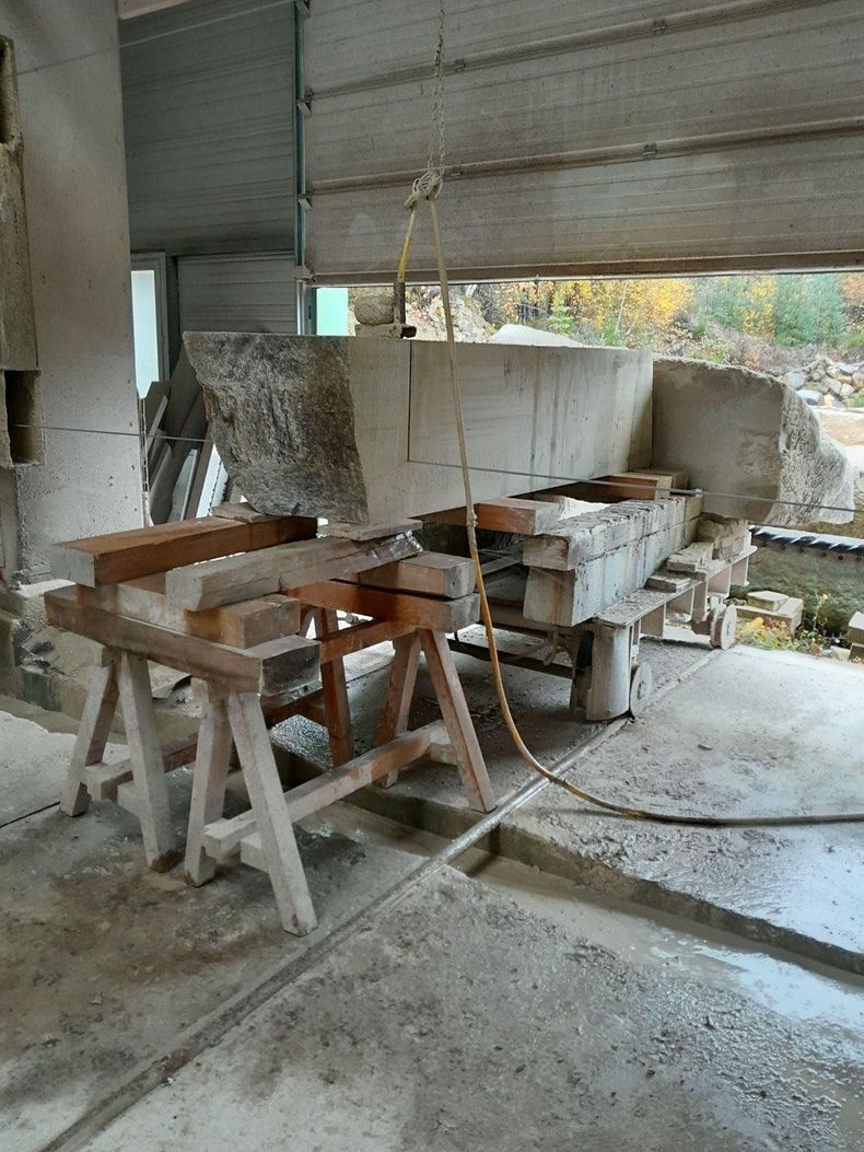 Atelier poussiéreux avec des pierres, des tréteaux et des outils sous un toit métallique partiellement ouvert