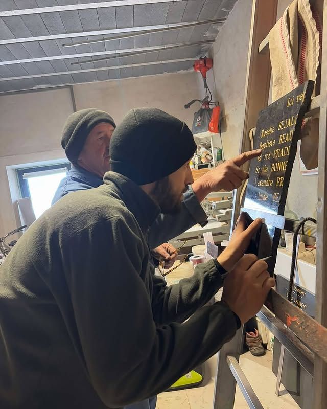 Deux ouvriers dans un atelier inspectent une plaque gravée posée un mur.