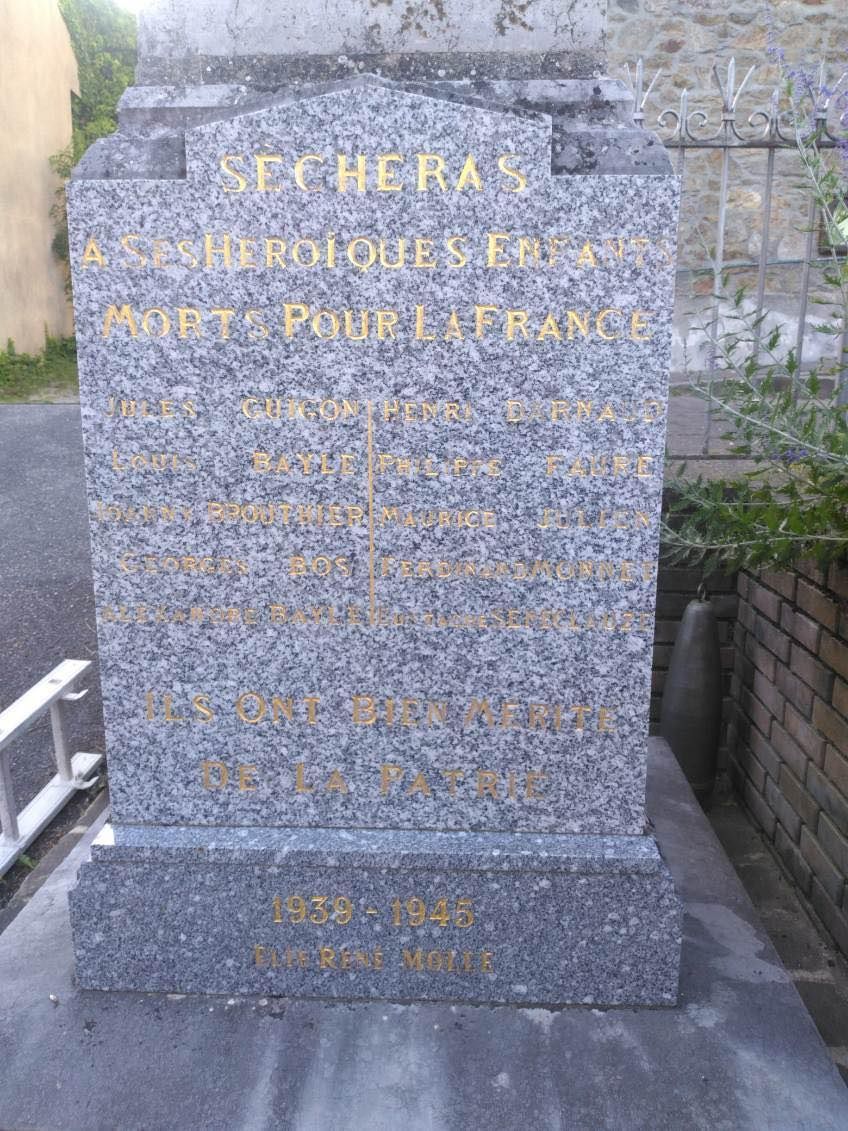 Plaque commémorative en pierre avec inscription dorée sur une terrasse en briques, visible à côté de marches et d'un mur.