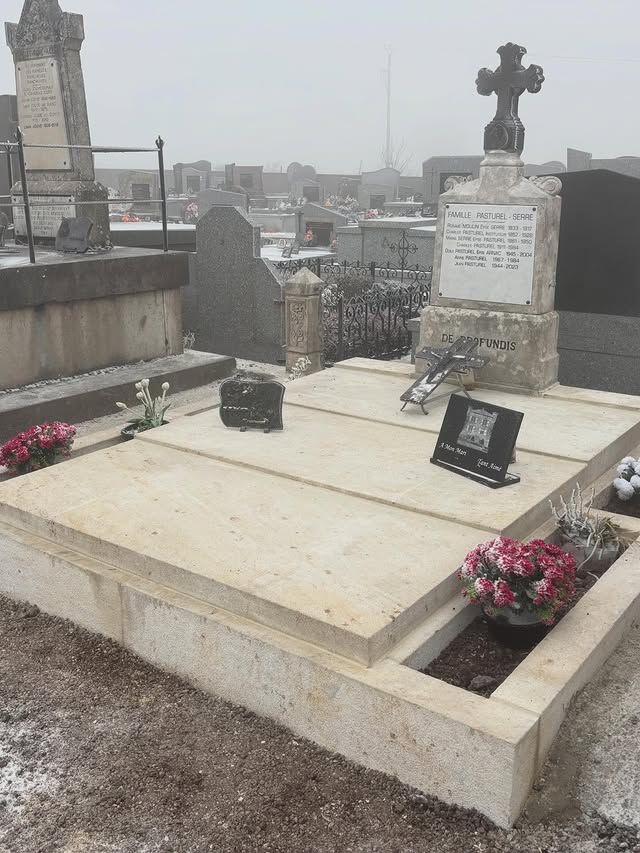 Tombe dans un cimetière, avec une pierre tombale surmontée d'une croix et des fleurs roses, par une journée d'hiver.