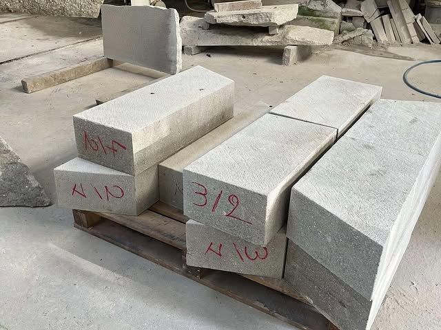 Des piles de blocs de pierre découpés dans un atelier, certains marqués en rouge avec des dimensions.