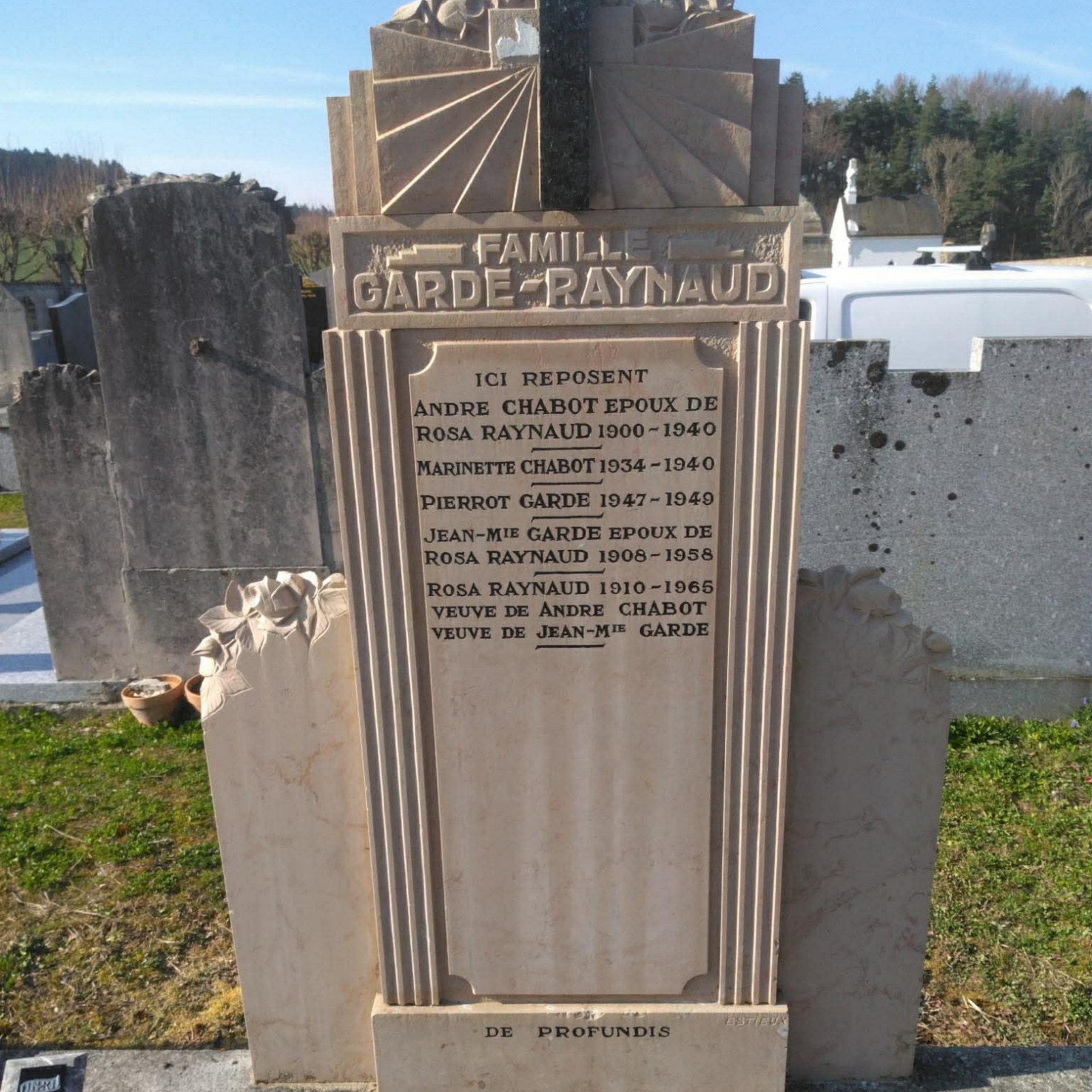 Plaque commémorative en pierre dans un cimetière, avec noms gravés et colonnes décoratives.