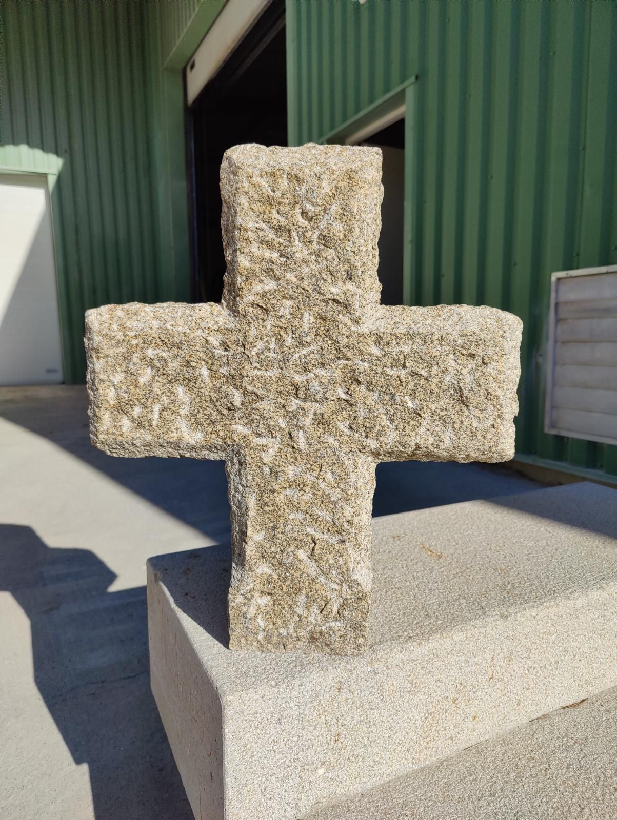 Sculpture en forme de croix en béton sur un piédestal devant un bâtiment écologique.