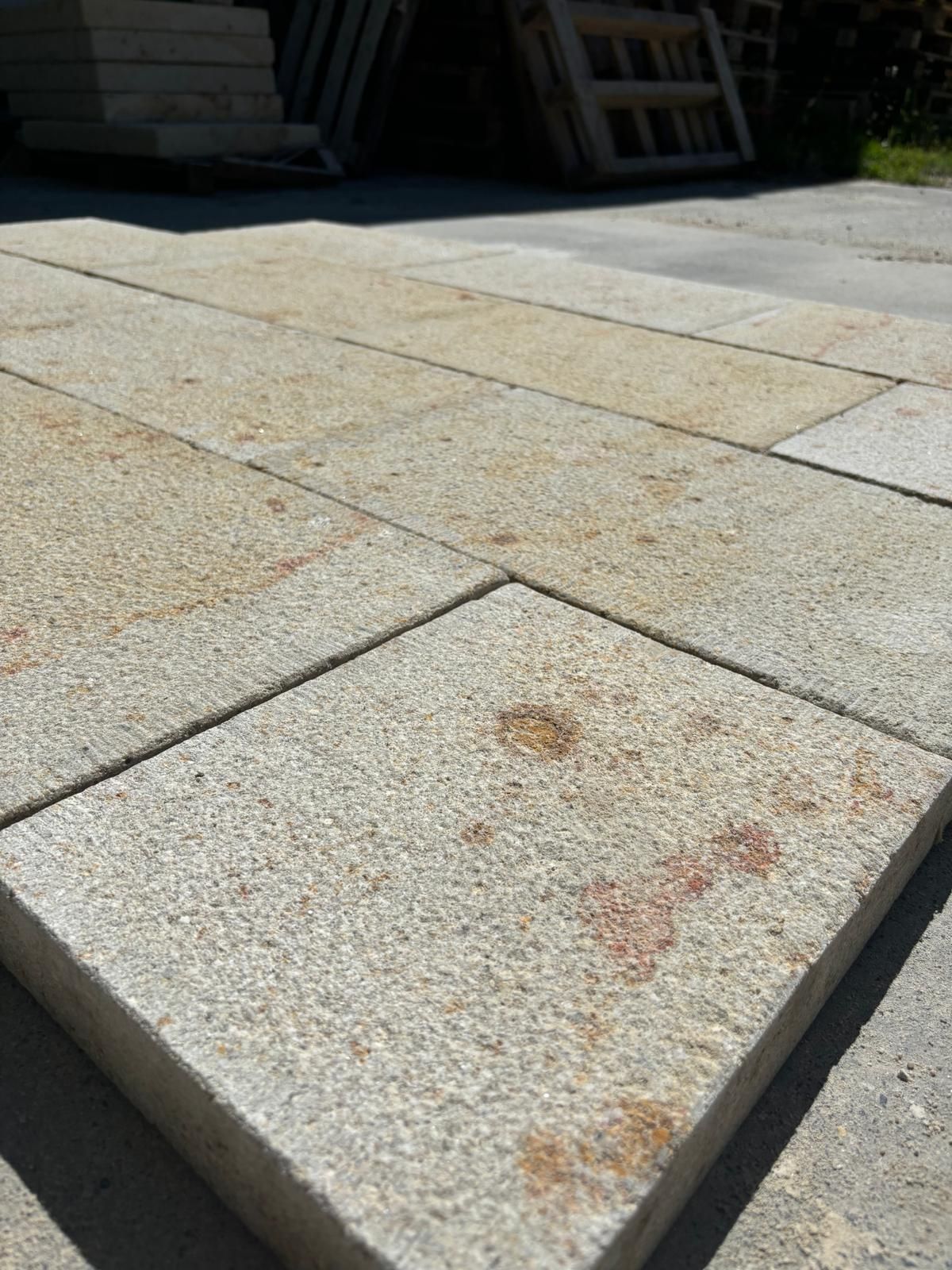 Dalle carrée rouillée parmi des carreaux de terrasse en pierre claire au soleil