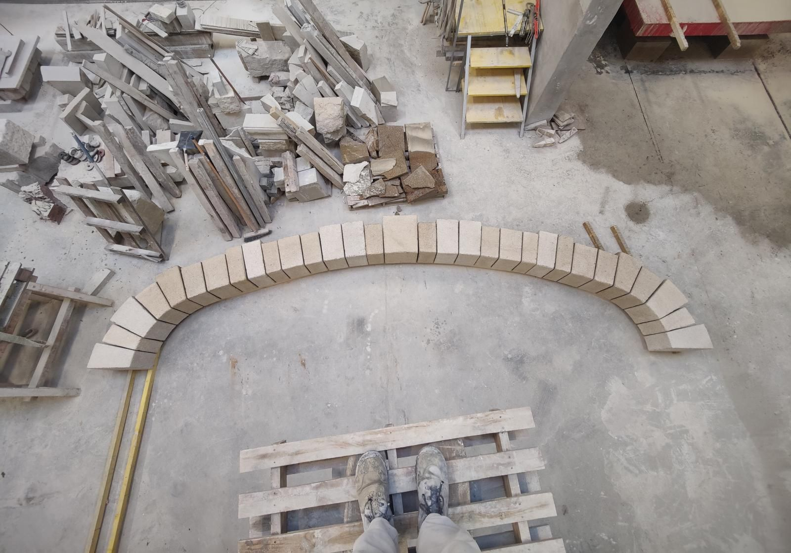 Rangée incurvée de blocs de béton clair sur un chantier de construction, avec des matériaux empilés à proximité.