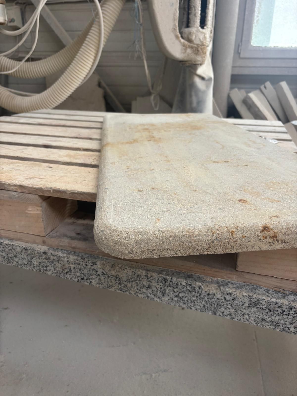 Une dalle blanche poussiéreuse repose sur une planche de bois à côté de tuyaux et de canalisations industrielles.