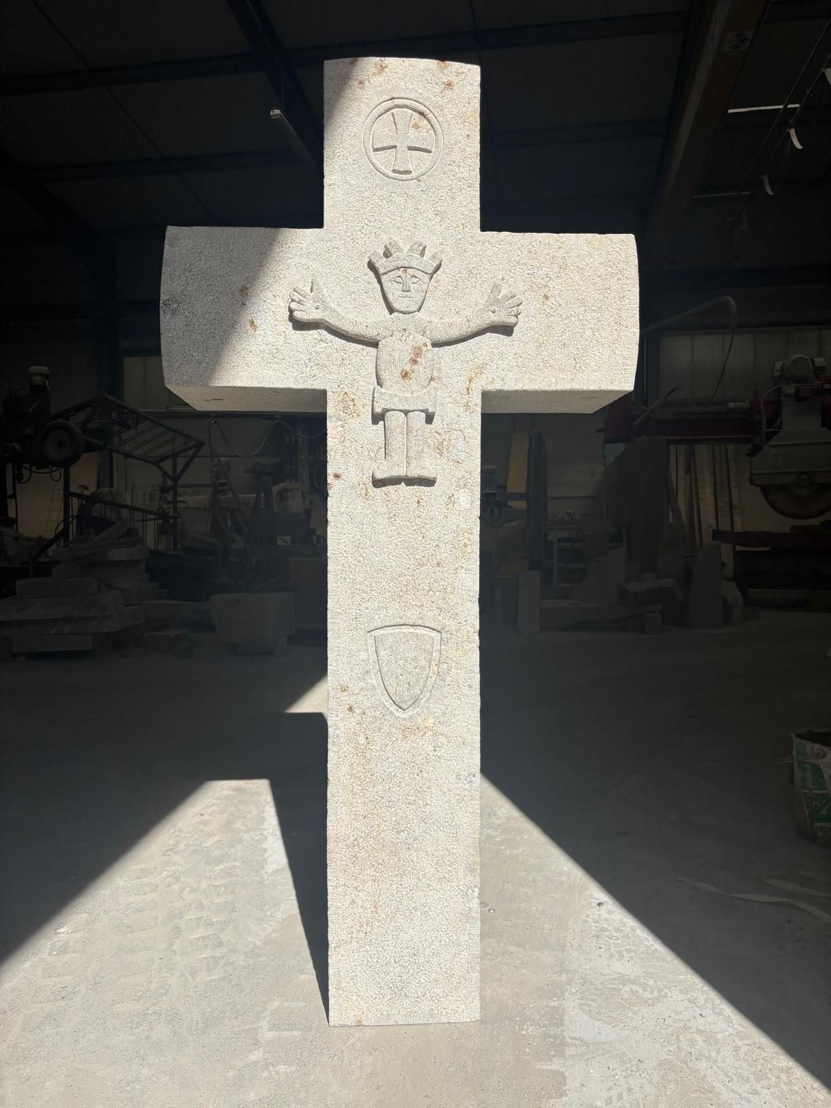 Croix de pierre avec un crucifix sculpté au soleil, dressée dans un espace intérieur sombre