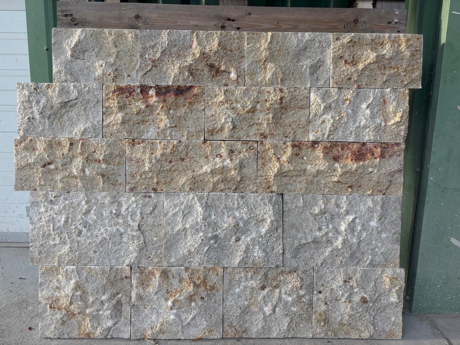 Mur en pierres grises empilées à côté d'une porte verte, avec une porte de garage blanche en arrière-plan.