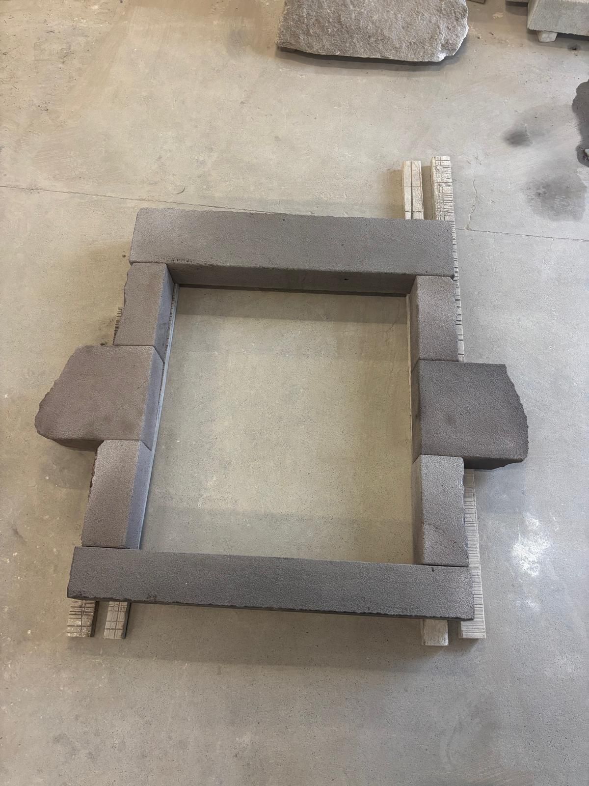 Cadre en blocs de béton sur le sol d'un atelier, avec deux panneaux latéraux et une ouverture rectangulaire au centre