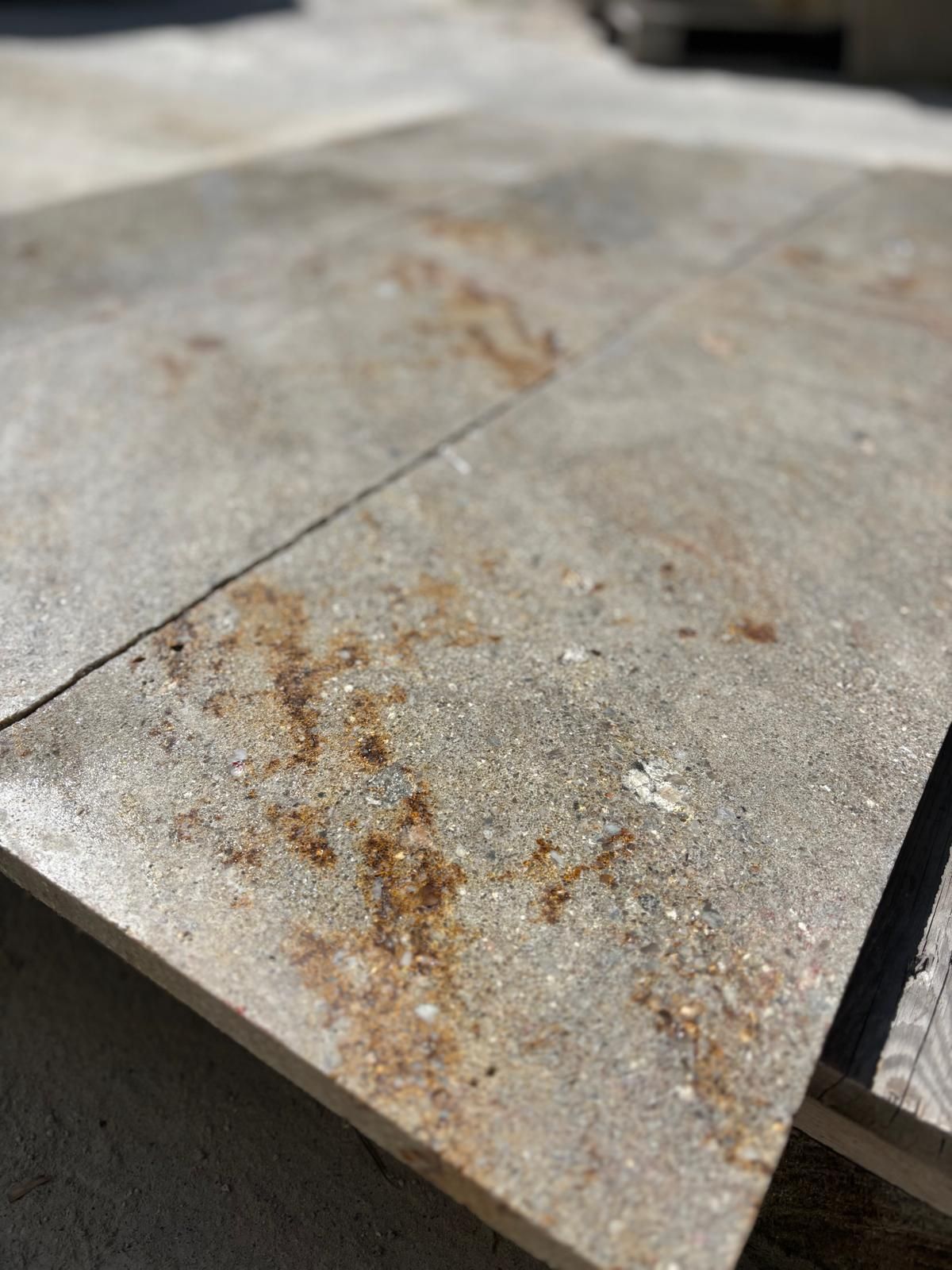 Gros plan sur un carreau gris fissuré présentant des taches couleur rouille et un bord en béton rugueux.
