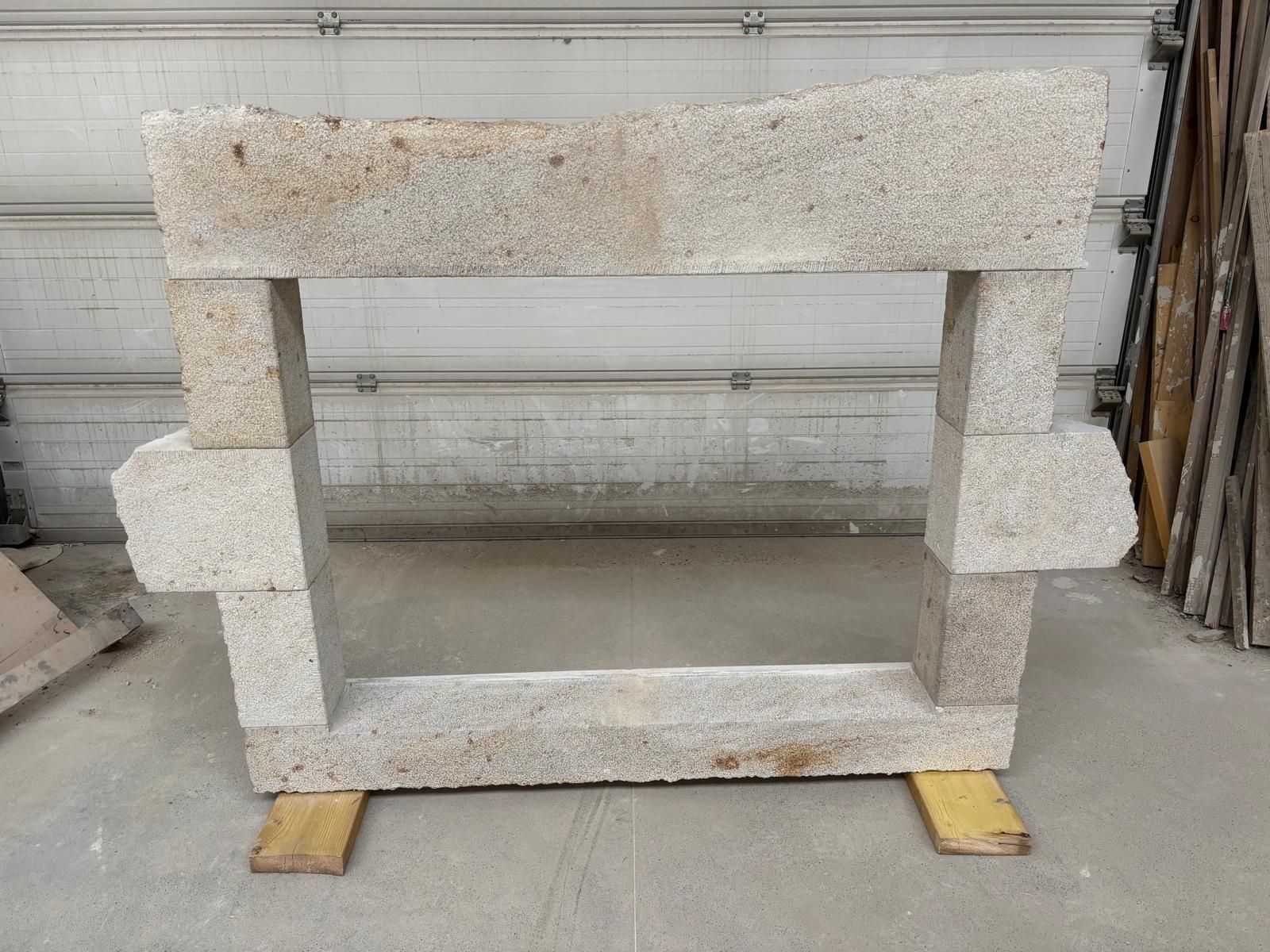 Grand cadre en pierre avec une ouverture rectangulaire, reposant sur des blocs de bois dans un entrepôt.