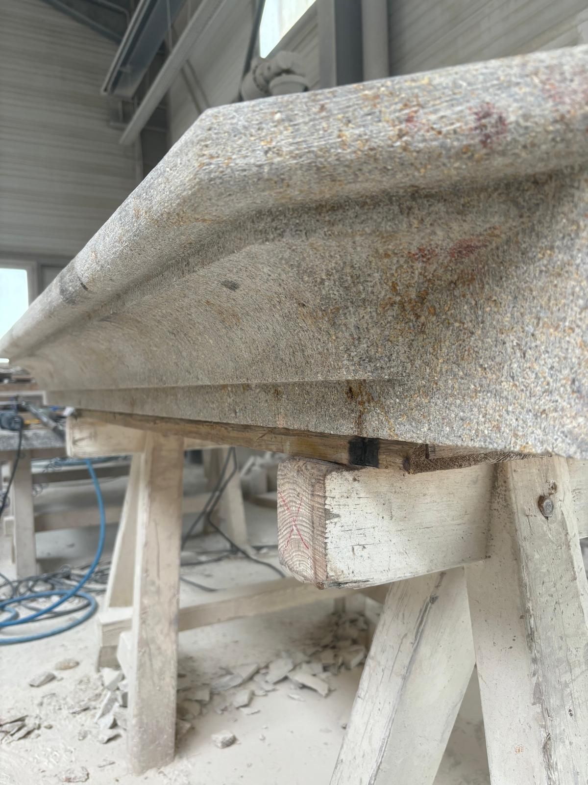 Dalle de pierre brute sur supports en bois dans un atelier, avec de la poussière et des outils à proximité