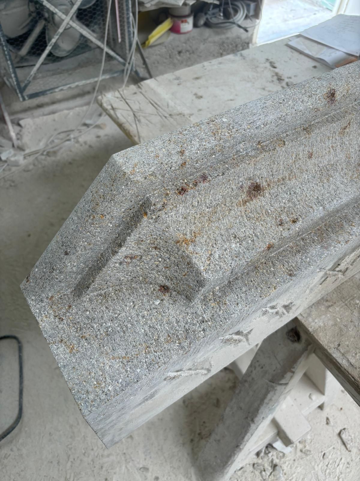 Dalle de béton brut à surface arrondie, posée sur le sol d'un atelier, entourée d'outils et de poussière.