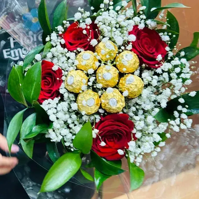 Una persona sostiene un ramo de rosas rojas y aliento de bebé.