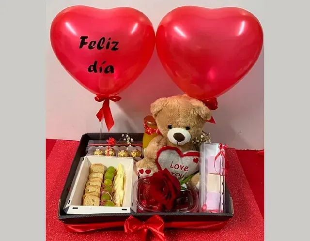 Una bandeja con un osito de peluche y globos que dicen feliz dia