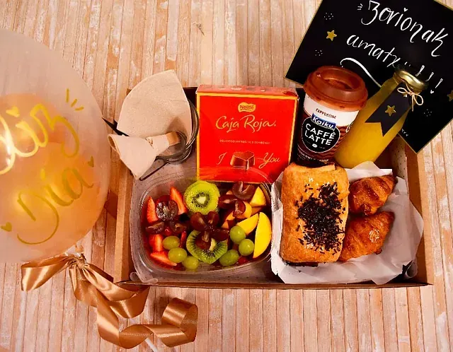 Una caja llena de una variedad de alimentos, incluidos croissants y frutas.