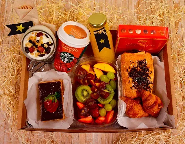Una caja llena de comida y bebidas, incluido un vaso de Starbucks.
