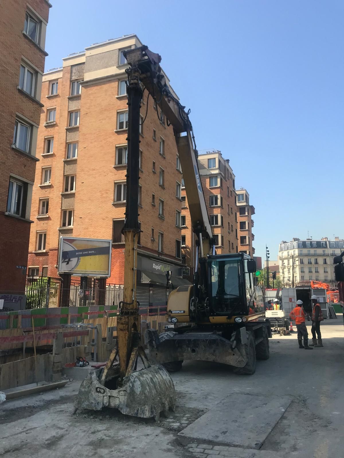 Une excavatrice creuse près d'un immeuble de plusieurs étages. Chantier de construction.