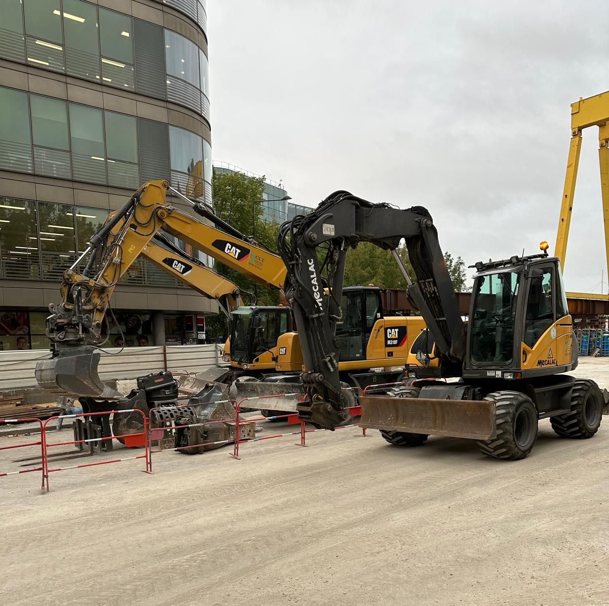 Chantier de construction avec trois excavatrices jaunes et noires travaillant près d'un bâtiment et d'une grue.