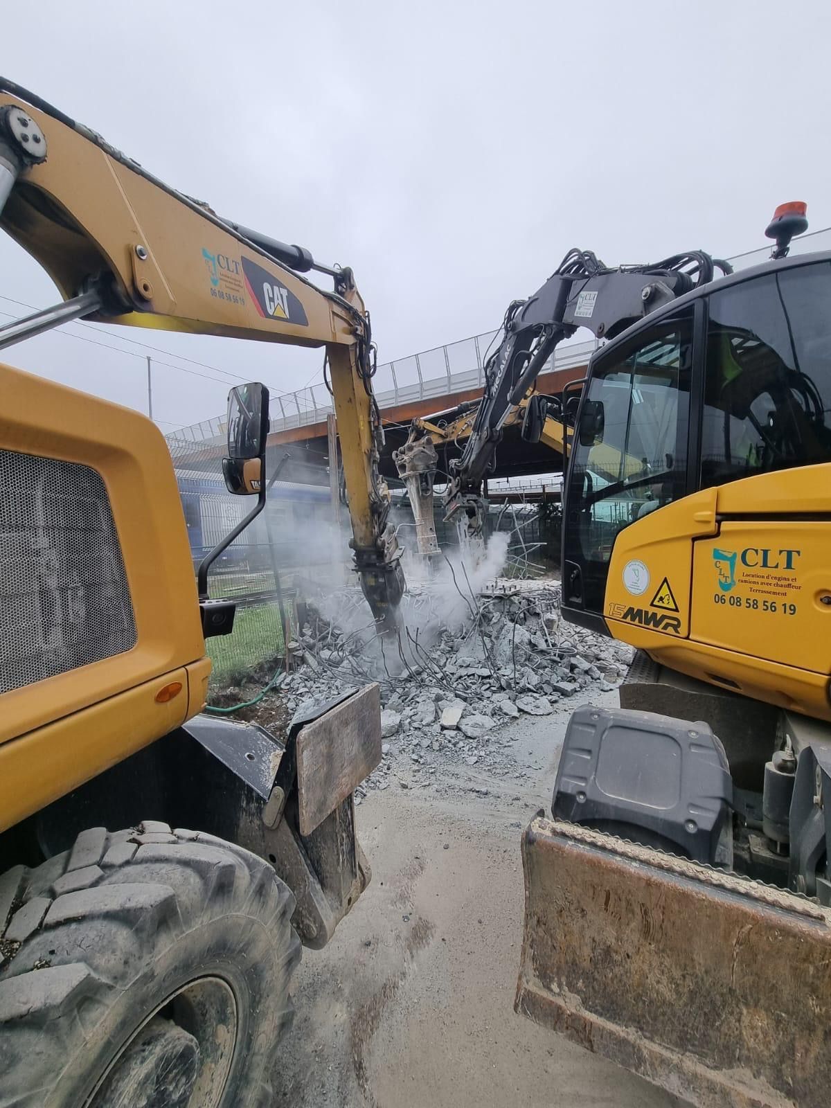 Deux pelleteuses jaunes démolissent une structure en béto.