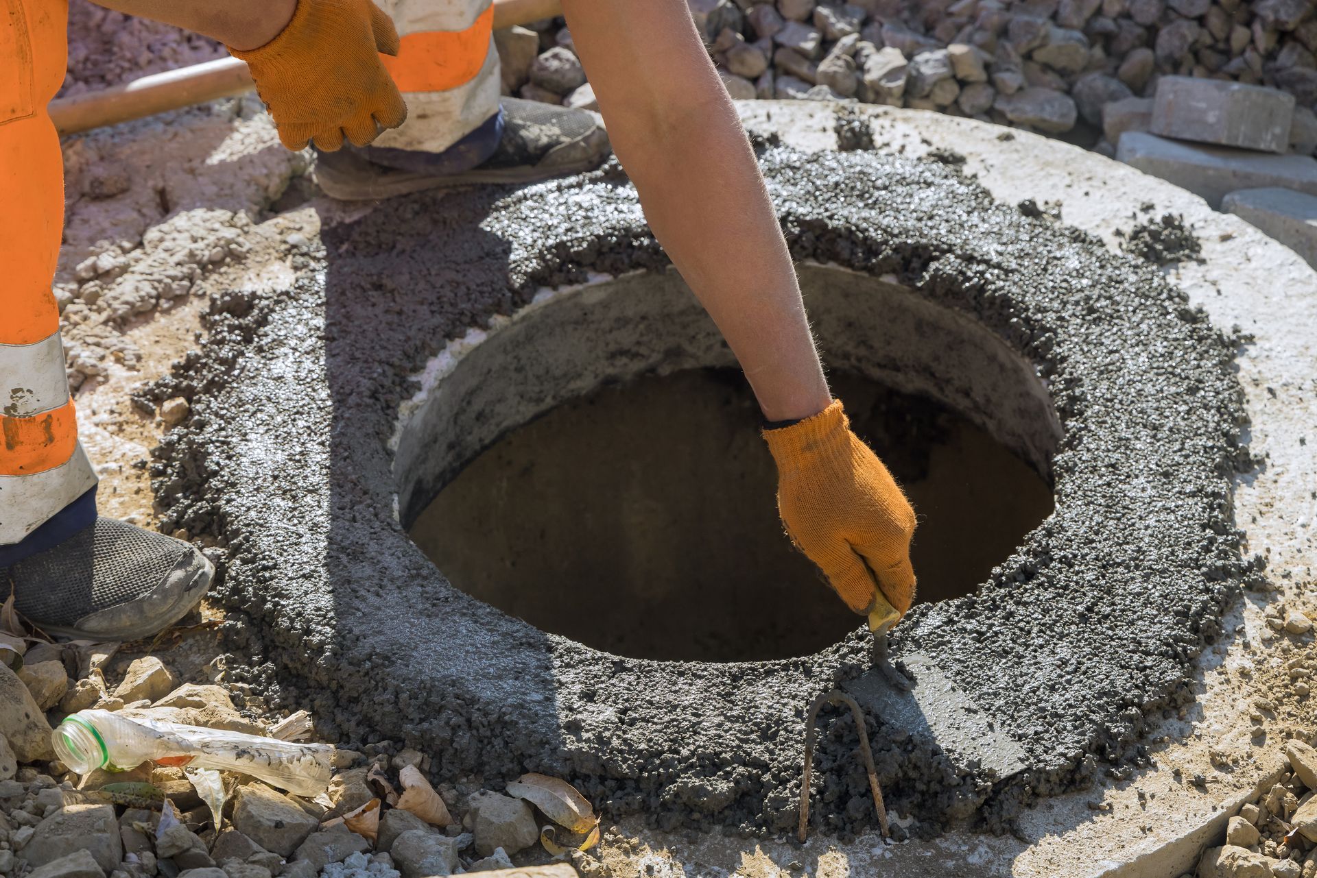 Personne en tenue de travail orange lissant le béton autour d'une ouverture de regard.