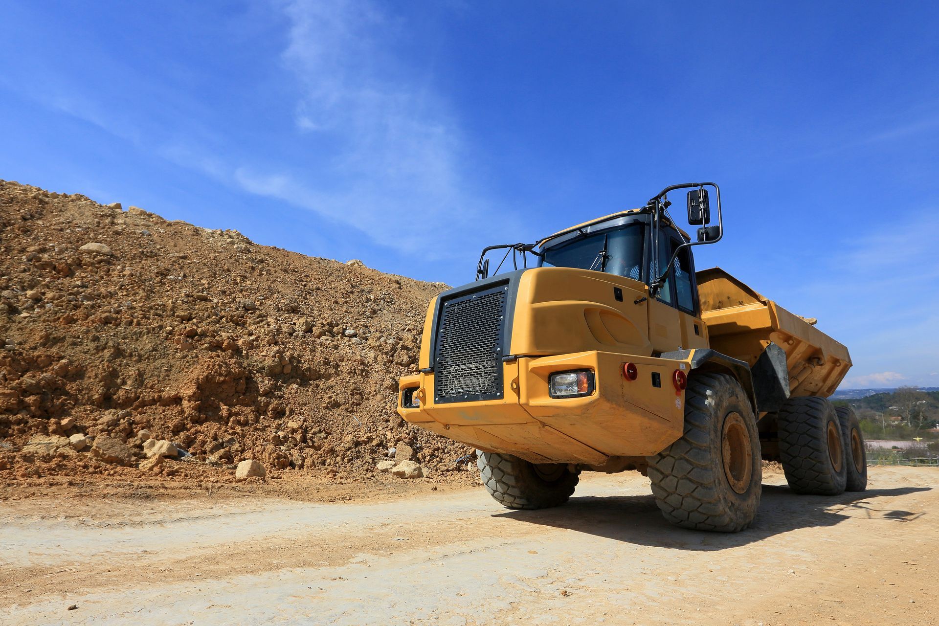 Un camion-benne jaune sur un chemin de terre, à côté d'un gros tas de terre.