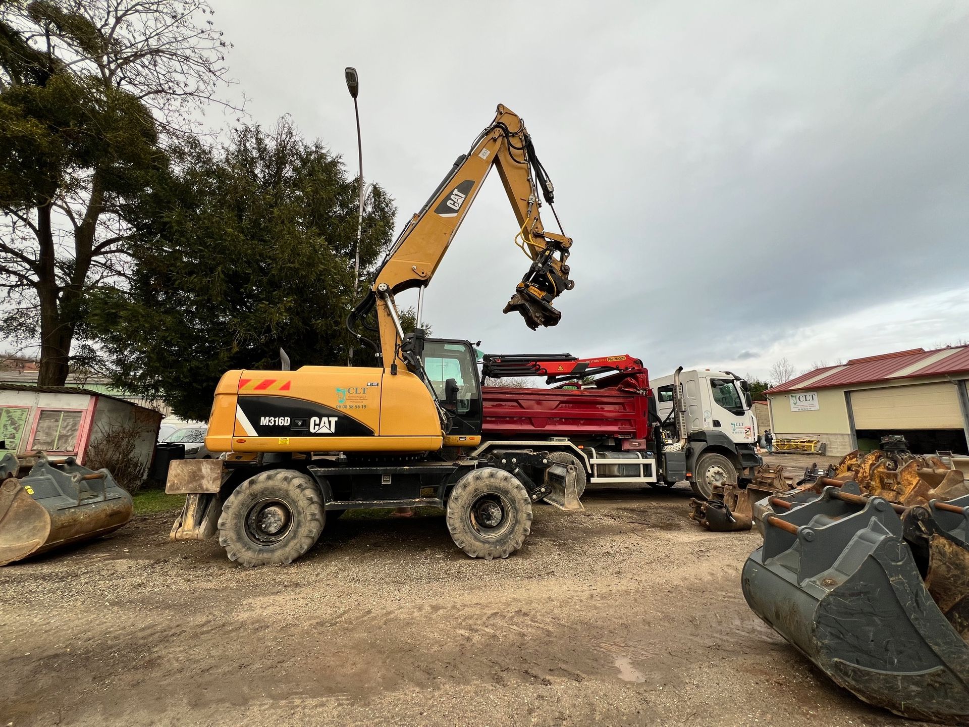 Une pelle mécanique CAT jaune charge un camion-benne rouge sur un terrain gravillonné sous un ciel couvert.