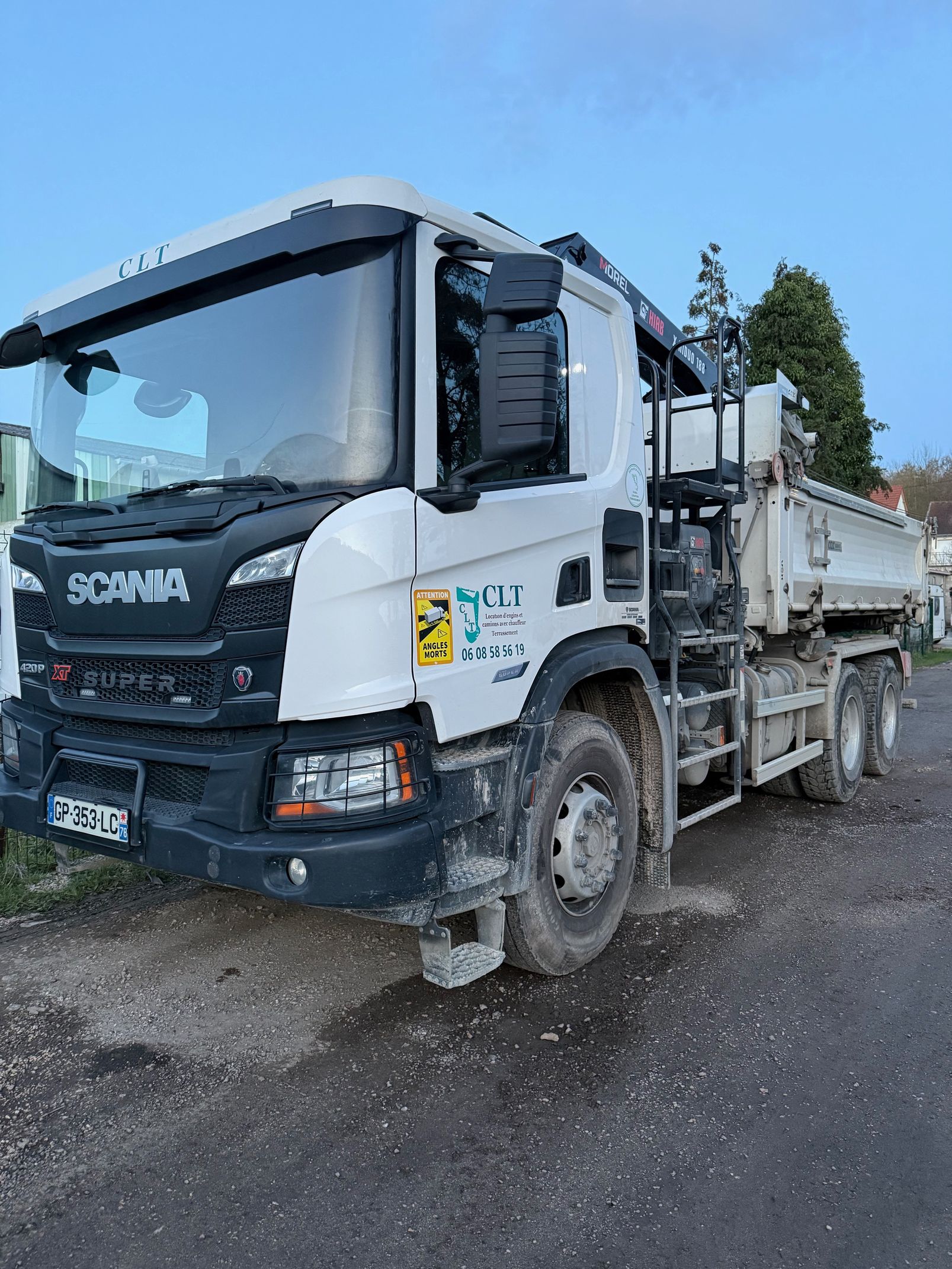 Camion-benne Scania blanc stationné à l'extérieur sur une surface gravillonnée.