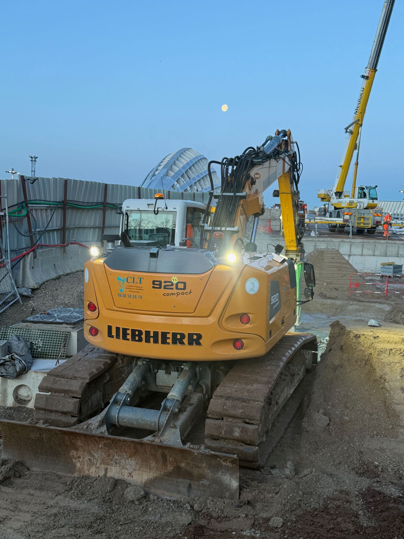 Une pelle mécanique Liebherr 926 jaune sur un chantier de construction au crépuscule.