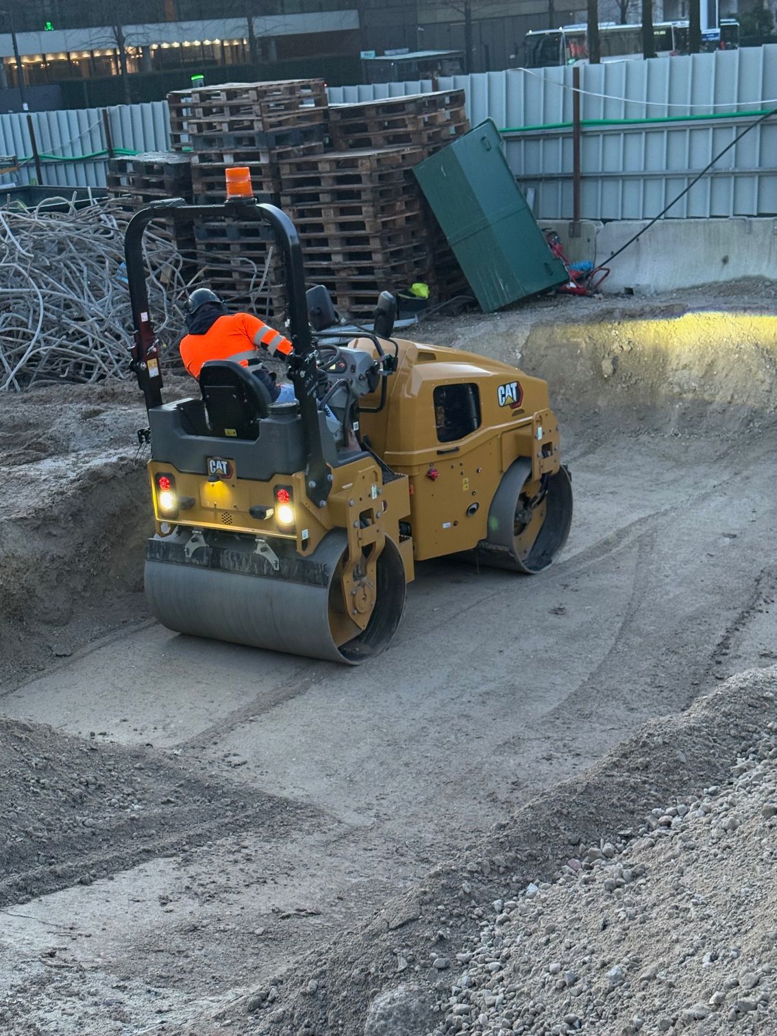 Un compacteur Caterpillar jaune sur un chantier de construction, en train de compacter le sol, avec une personne à son bord.