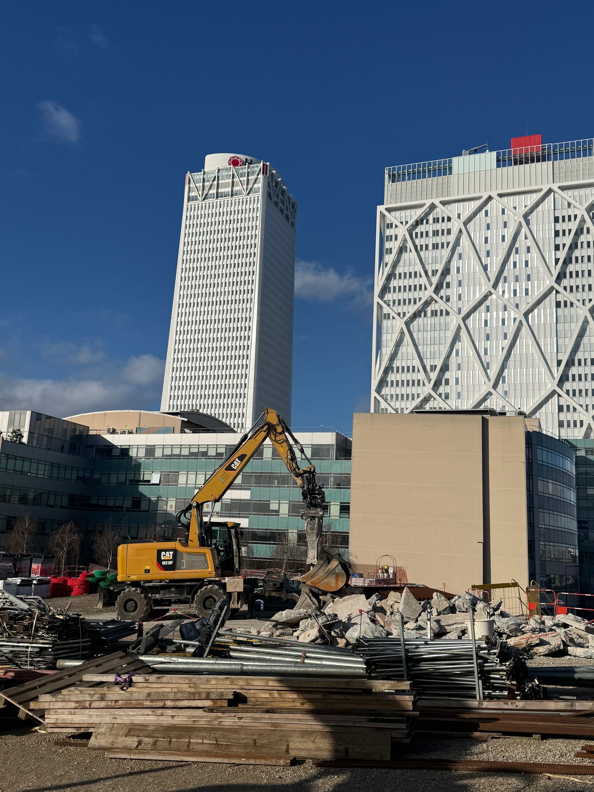 Chantier de construction avec une excavatrice démolissant des débris devant deux gratte-ciel.