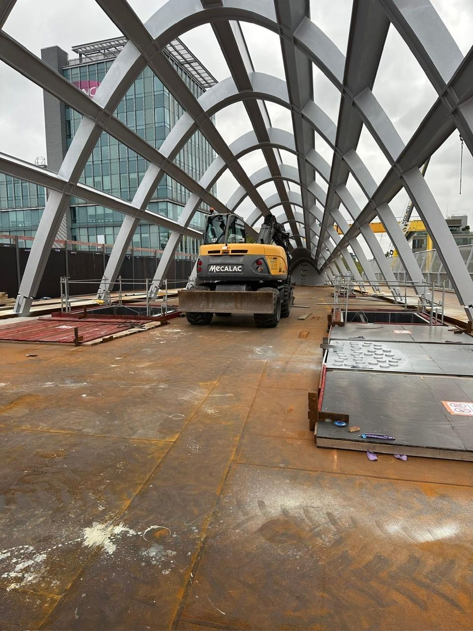Chantier avec une pelleteuse jaune à l'intérieur d'une structure métallique voûtée.