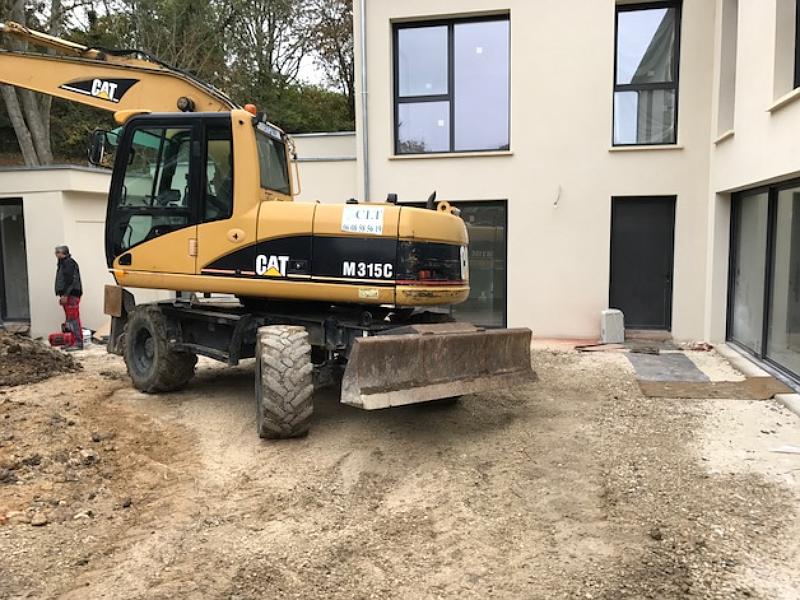 Une pelle à pneus 17T mécanique jaune de type CAT sur un chantier de construction, à côté d'un bâtiment.
