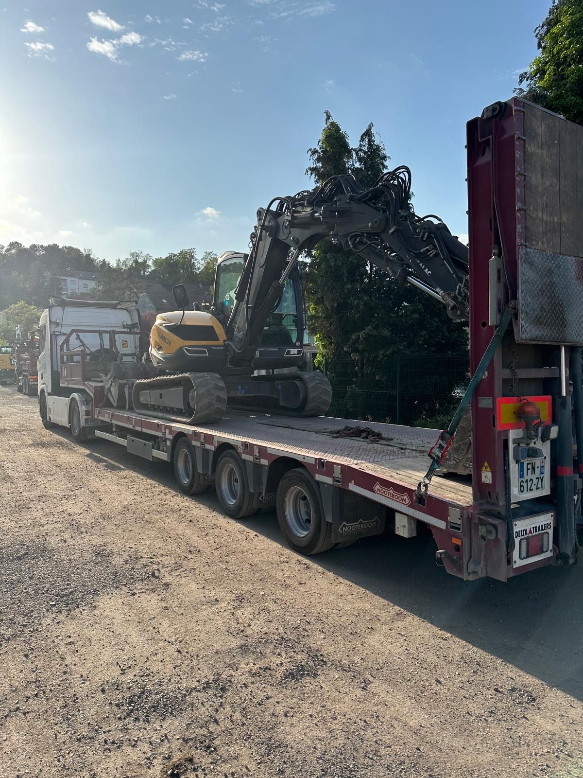 Une excavatrice sur une remorque à plateau, stationnée sur un chemin de terre.