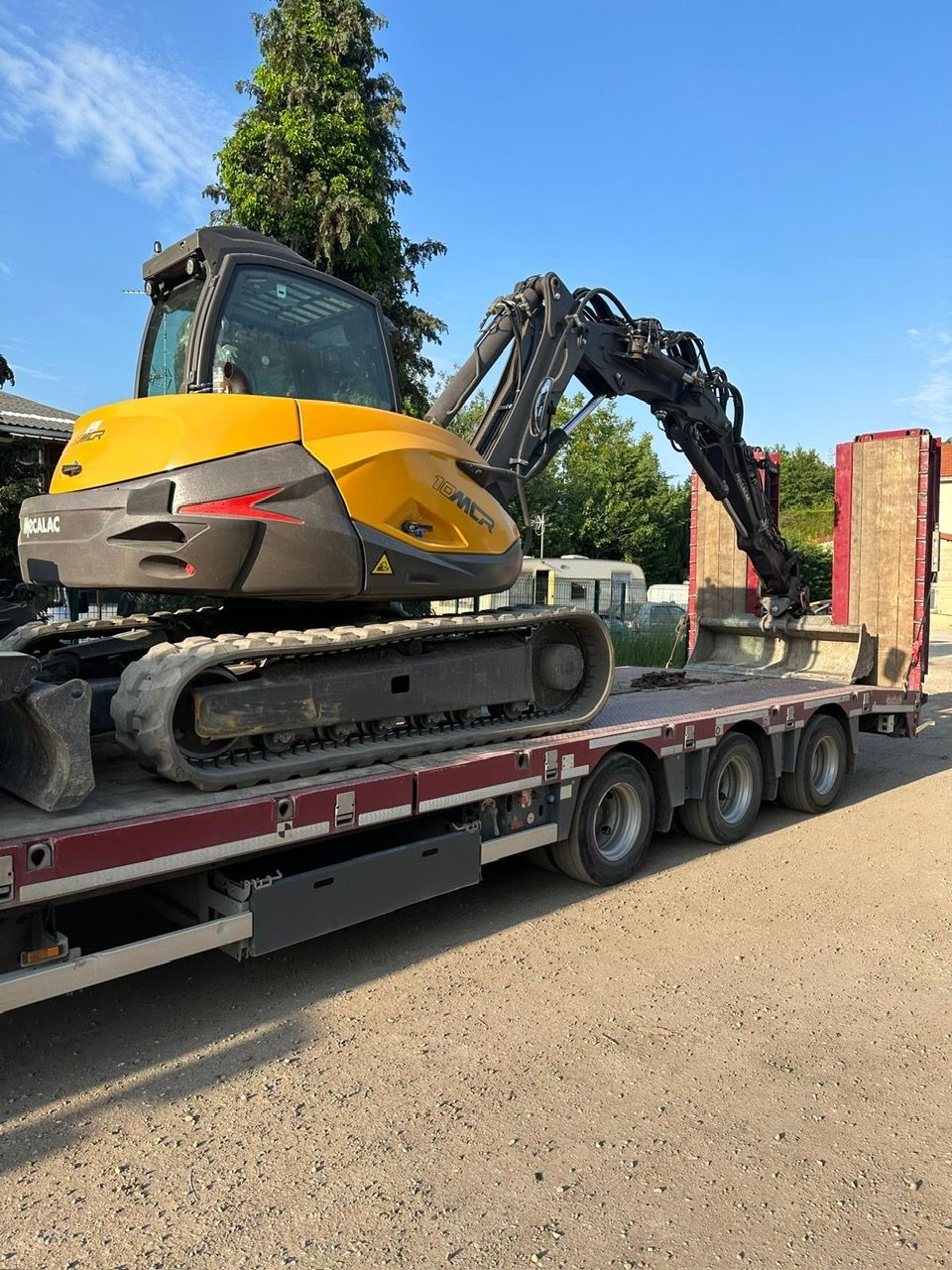 Une pelleteuse jaune sur une remorque rouge, prête à être transportée.