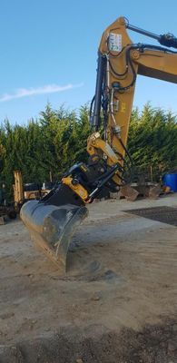 Bras et godet d'une excavatrice jaune sur un sol terreux : tiltrotateur.