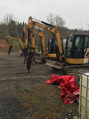 Trois excavatrices jaunes (pelles à chenilles) sur du gravier, dont une équipée d'un marteau-piqueur.